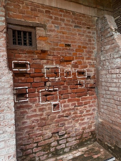 Original bullet holes preserved on the red brick wall at Jallianwala Bagh, framed by white squares